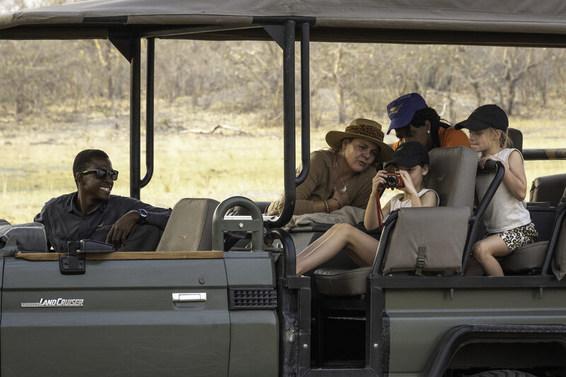 A woman and children in a safari vehicle looking at a camera held by a young girl.