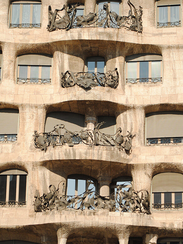 Close-up of four levels of the wavy stone facade and organic wrought-iron balconies of Casa Batlló, for luxury Spain holidays.