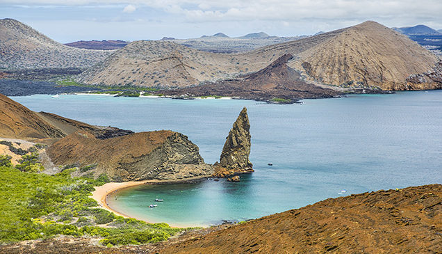 Striking Pinnacle Rock geological formation in the foreground of a turquoise bay, surrounded by arid volcanic hills. luxury Galapagos tours.
