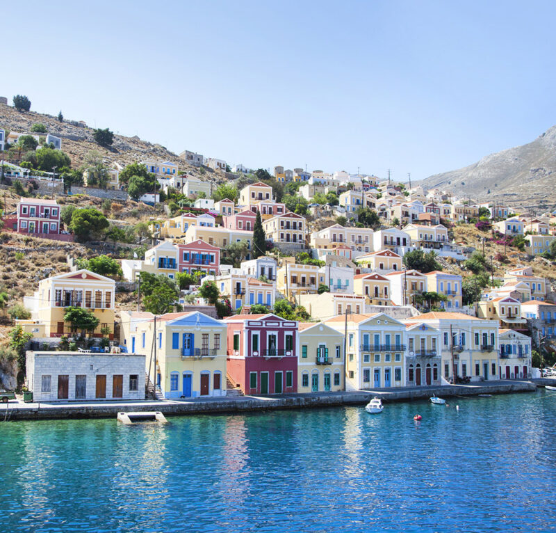 Luxury Greece Tours - Beautiful city of Symi, Greece, with colourful cube-shaped buildings lining the waterfront