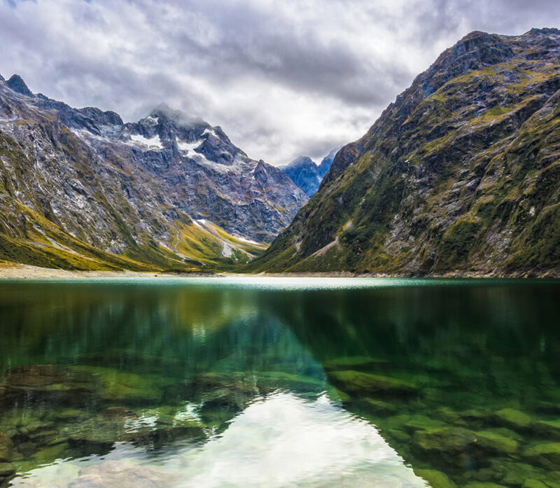Dramatic mountain peaks reflected in the still water of a glacial lake on luxury New Zealand vacations.