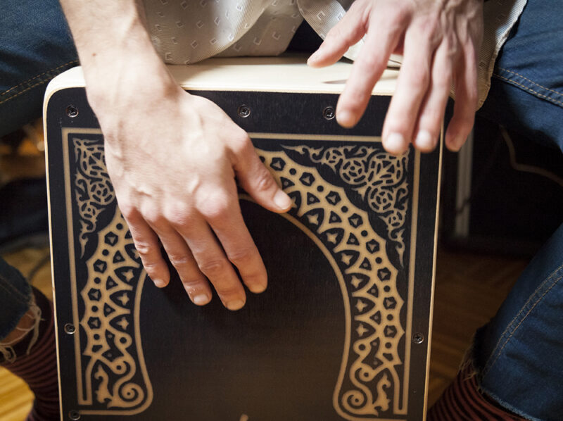 Close-up of a person's hands playing the top of a decorated wooden cajon drum, a sound of luxury Portugal vacations.