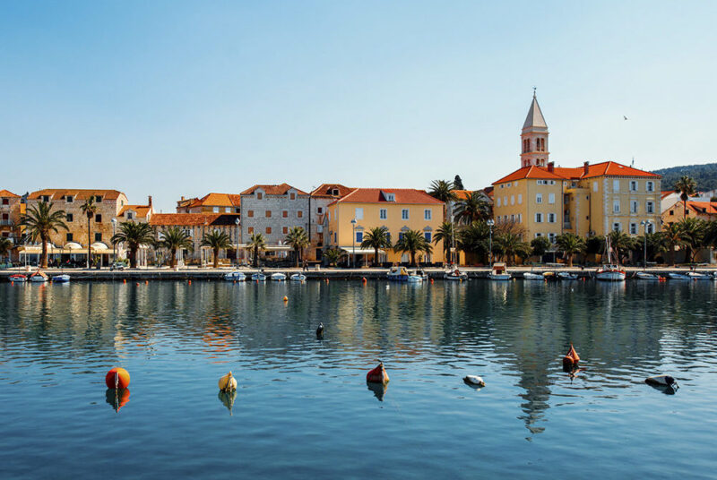 Waterfront buildings and palm trees reflected in a calm harbor during luxury Croatia trips.