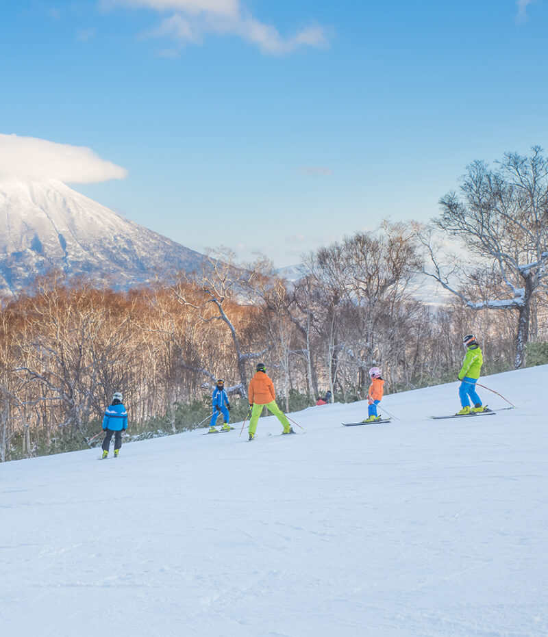 A group of skiers descends a snowy slope with a large mountain in the distance during luxury family trips to Japan.