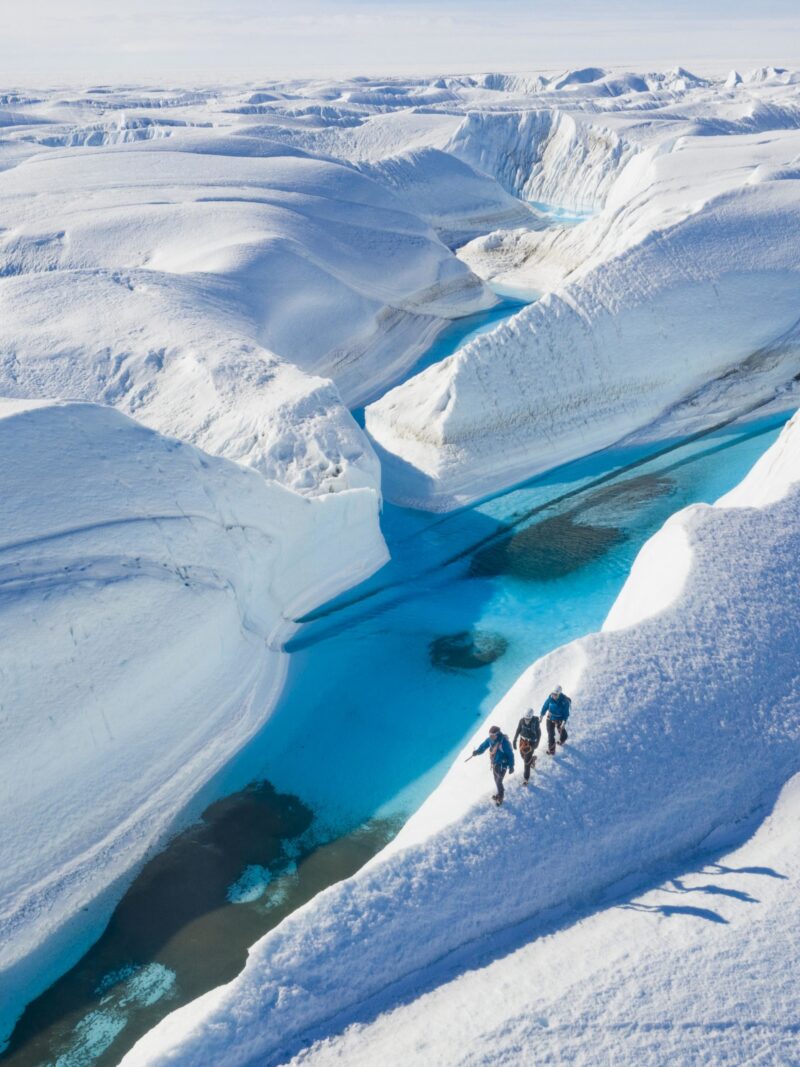 Aerial view of hikers on snow ridges by turquoise water, featured on luxury Polar trips.