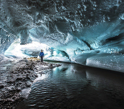 A person exploring a large ice cave with frozen ripples, part of Luxury Polar tours.