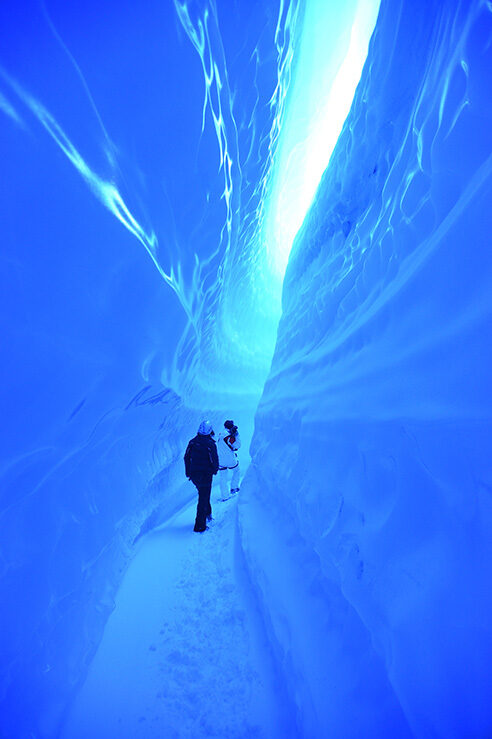 Two people walking through a vibrant blue ice cave, an activity offered on luxury Polar vacations.
