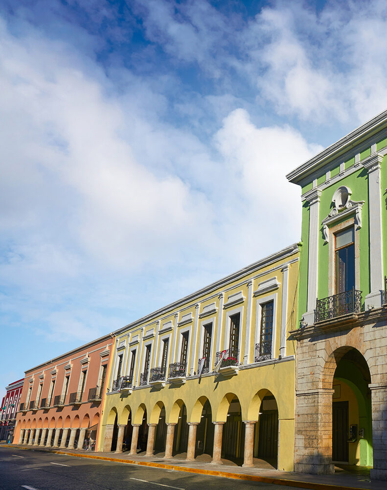 A street lined with a row of brightly colored colonial buildings with arches and balconies, found on luxury Mexico vacations.