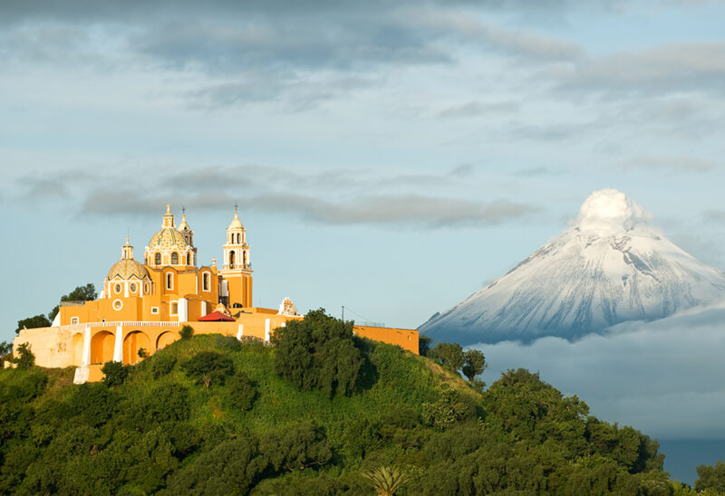 ellow church on a green hill with a snow-capped volcano visible behind it, often seen on luxury Mexico tours.