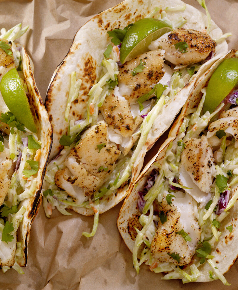 Three grilled fish tacos on flour tortillas with cabbage slaw, cilantro, and lime wedges, perfect for luxury Mexico tours.