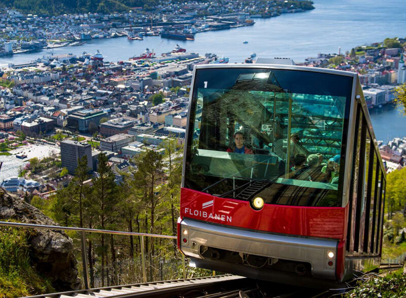 The red Fløibanen funicular going up a steep slope with a panoramic view of the city of Bergen below, available on luxury Norway holidays.
