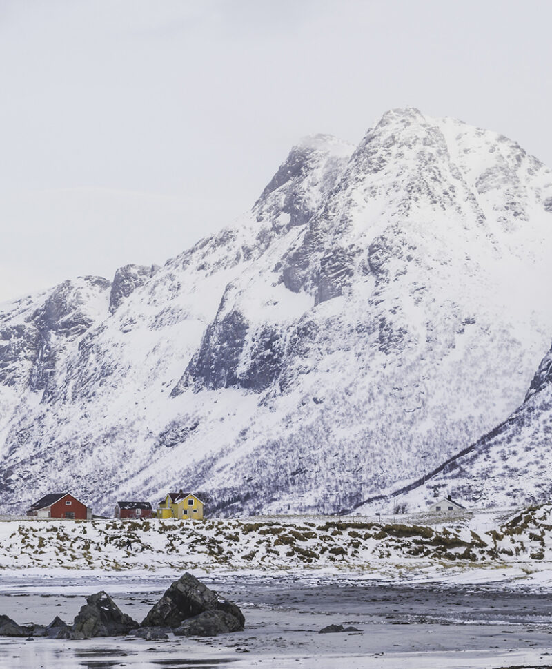 Large snow-covered mountains towering over small, colorful cabins in a winter landscape, perfect for luxury Norway vacations.