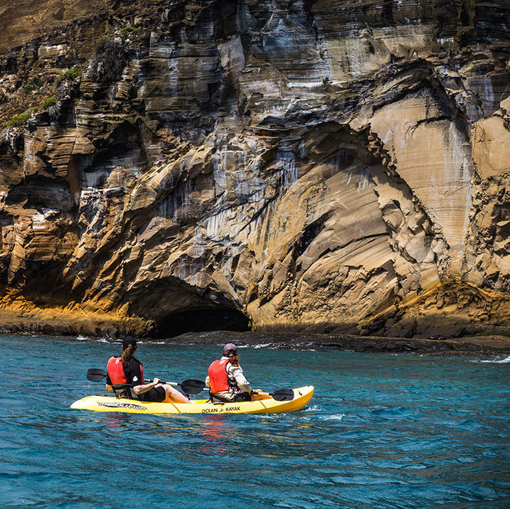 Two people kayaking past a sea cave on luxury Galapagos family tours.