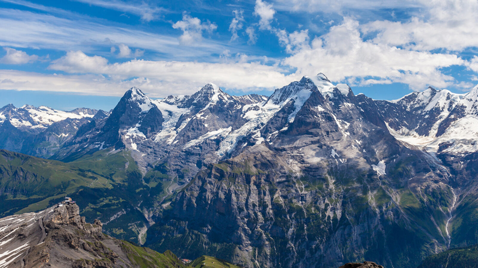 High altitude panoramic view of jagged snow-dusted mountain ranges under a blue sky on luxury Switzerland vacations.