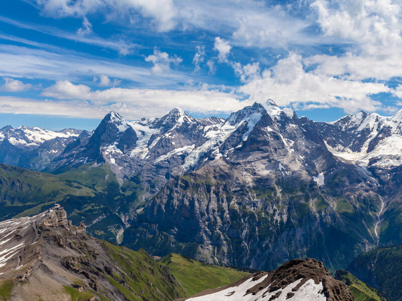 High altitude panoramic view of jagged snow-dusted mountain ranges under a blue sky on luxury Switzerland vacations.