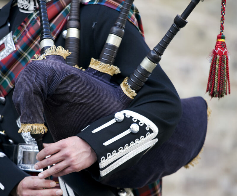 Close-up of a person in tartan holding and playing the bagpipes, with gold and silver trim visible. Experience this on luxury Scotland vacations.