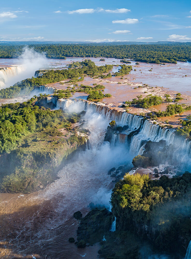 Panoramic aerial view of the massive Iguazu Falls, showing powerful cascades surrounded by green forest. luxury Brazil tours.