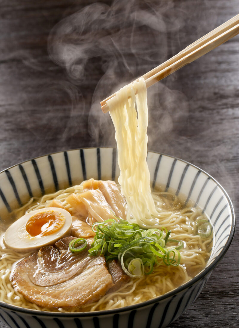 Close up of chopsticks lifting noodles from ramen broth in a decorative bowl