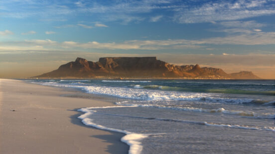 Sandy beach with ocean waves and Table Mountain in the distance on luxury Cape Town trips.