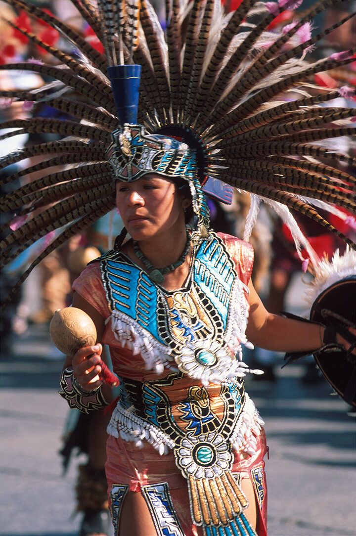 A person in a large feathered headdress and traditional turquoise dress on luxury Latin America honeymoon tours.