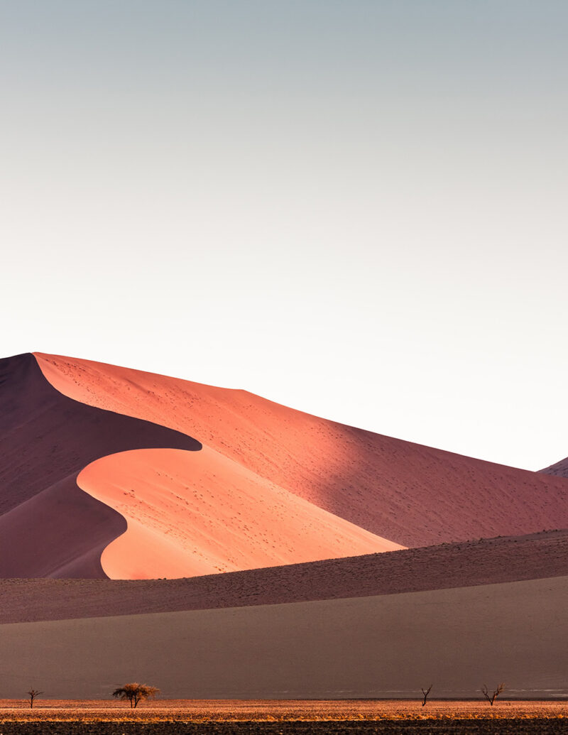 Vibrant red and orange sand dunes under a clear sky, seen on luxury Africa honeymoon vacations.