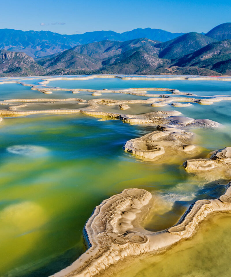 Striking travertine rock terraces and pools of Hierve el Agua with aqua and green water, backed by distant mountains, luxury Latin America grand tour holidays.