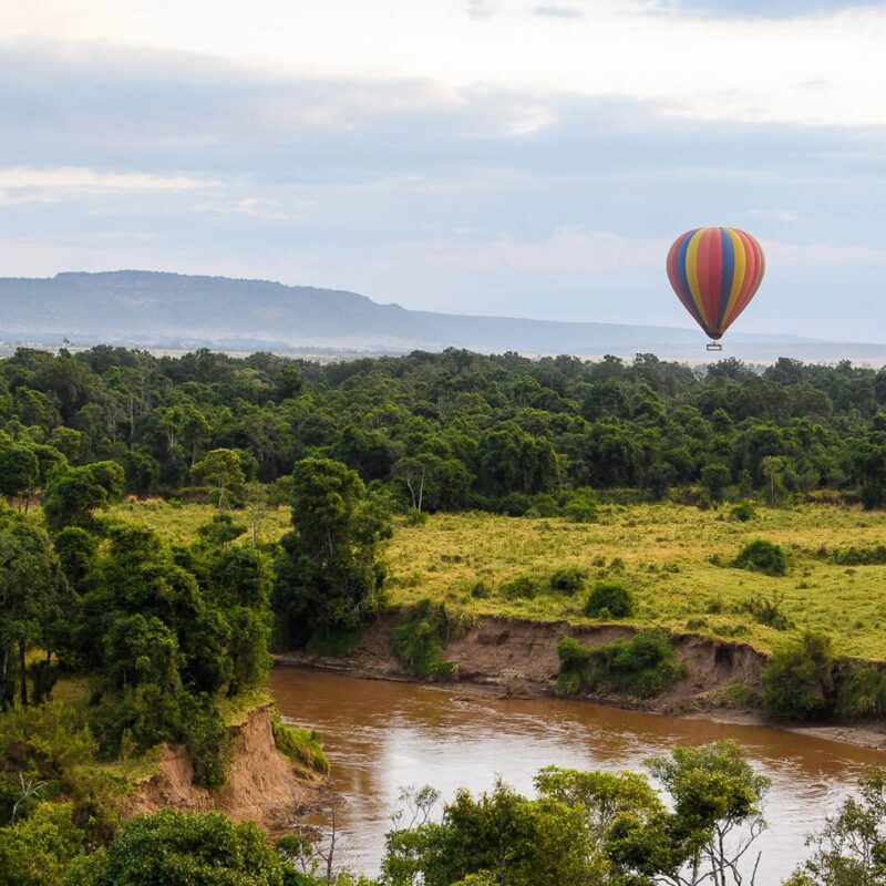 A hot air balloon drifting over a scenic river bend during luxury Maasai Mara holidays.