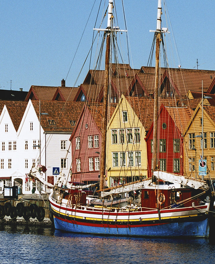 Old fishing buildings by the harbour in Bergen, Norway, with a tall mast ship docked next to them