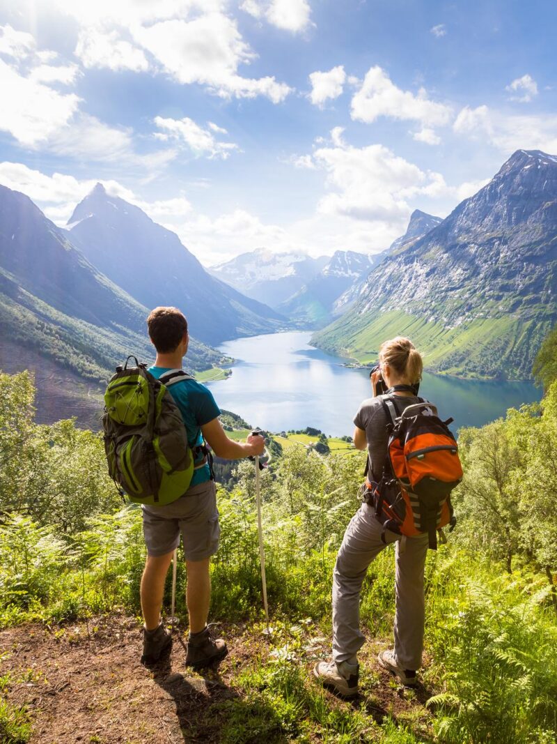 Two hikers at viewpoint in the mountains enjoying beautiful view of the valley with a lake and sunny warm weather in summer, green trees around 814397912 active, adventure, amazing, backpack, beautiful, blue sky, couple, enjoying, fjord, girl, green trees, happiness, happy, hike, hikers, hills, holidays, incredible, lake, man, mountains, nature, norway, outdoors, panorama, panoramic, people, person, photographing, sea, summer, sun, sunny, sunshine, travel, travelers, trek, trekkers, two, vacations, valley, view, viewpoint, wanderlust, warm, water, white clouds, wilderness, woman, young Norwegian Fjords, Norway