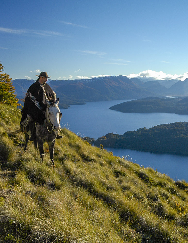A person riding a horse on a high grassy path above a blue lake