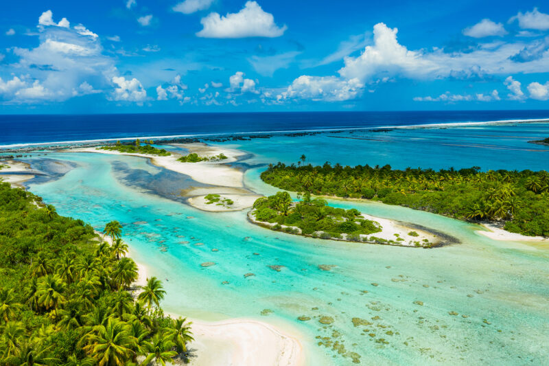 Aerial view of lush green tropical islands and clear blue water channels on luxury French Polynesia trips.