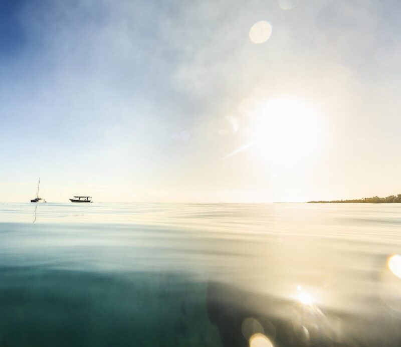 Bright sun reflecting on calm sea water with boats on the horizon during luxury French Polynesia holidays.