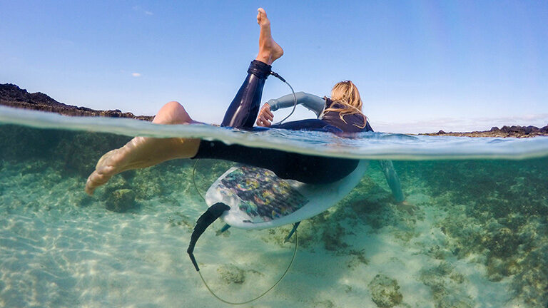 Split level view of a person on a surfboard over a clear sandy seabed on luxury French Polynesia tours.