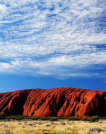 Red sandstone ridges of Uluru anchor the desert floor beneath open skies in Australia's Red Centre.