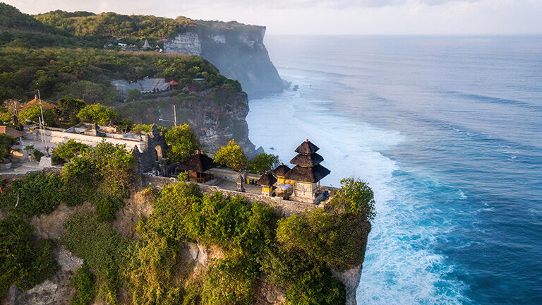 Coastal Balinese temple on a high cliff above blue ocean waves during luxury grand tours.
