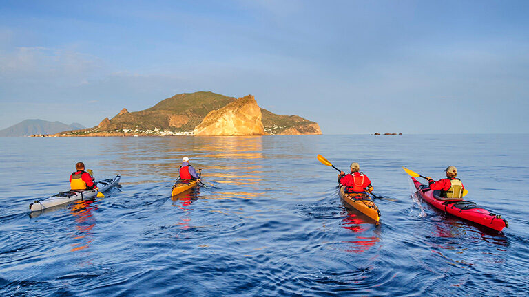 A group of people kayaking in the sea with a small green island behind