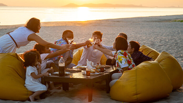 Group of multiethnic family friends enjoy dinner party together on the beach at sunset.