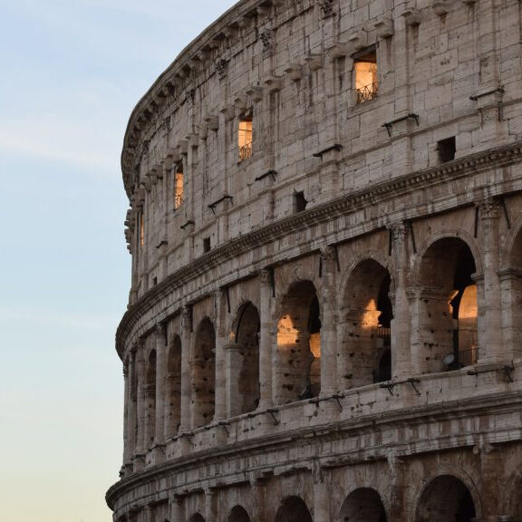 Golden evening light glows through the ancient stone archways of Rome's Colosseum.