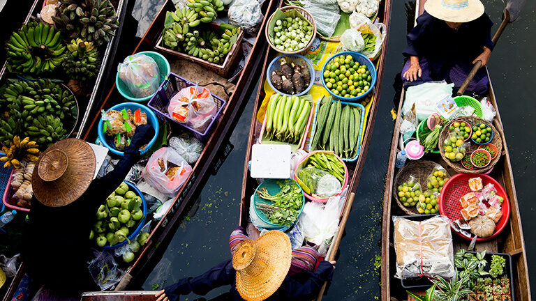 Aerial view of several boats filled with fresh produce at a traditional floating market. luxury food and wine trips.