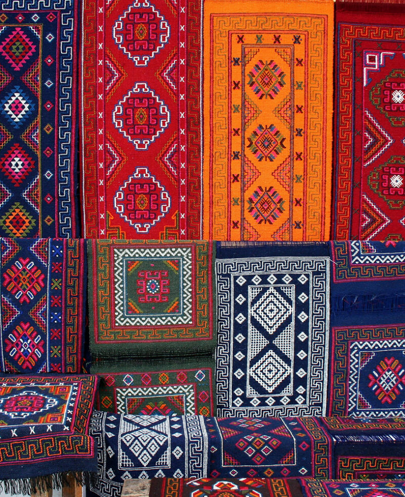 Close-up of various colorful patterned Bhutanese textiles hanging in vertical and horizontal rows.