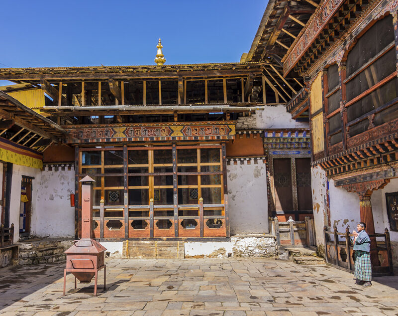A person stands in a stone courtyard before a large traditional building with ornate wooden window frames.