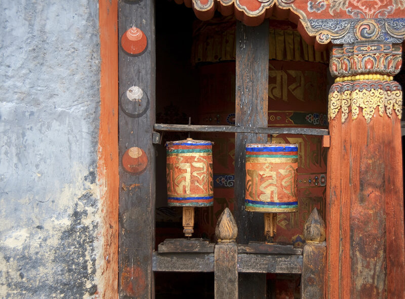 Close-up of two ornate, colorful prayer wheels mounted on a wooden frame within a traditional structure.