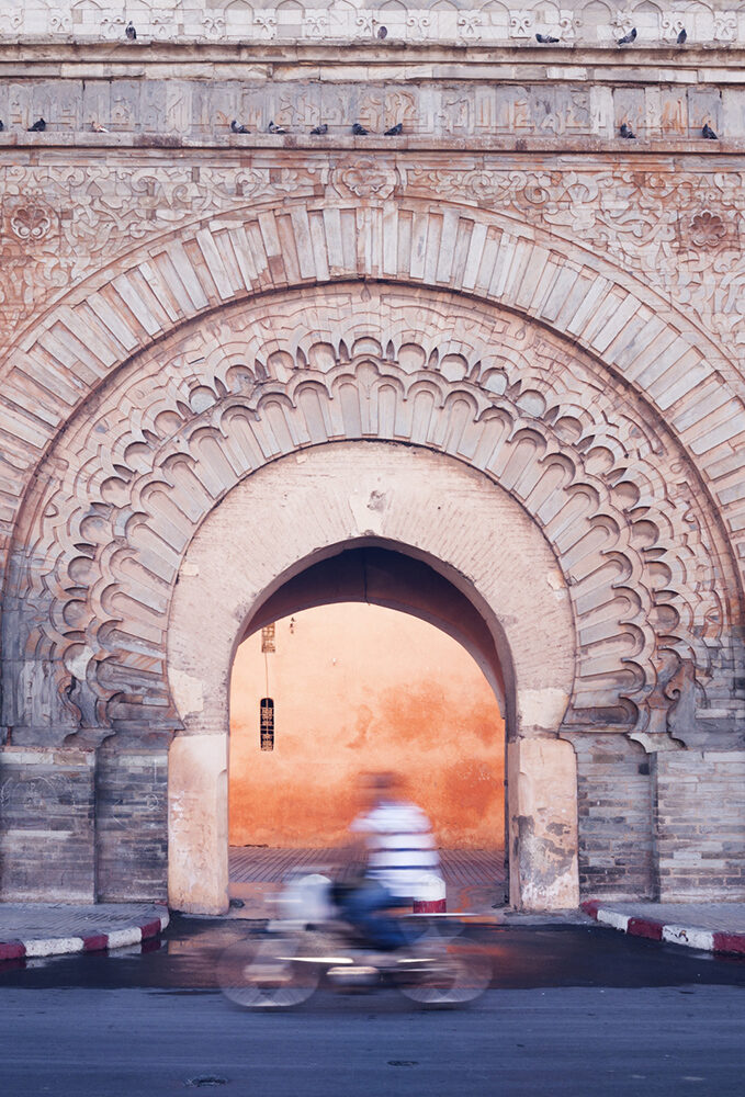 A motorist blurs past Bab Agnaou’s ornate stone archway in Marrakech.