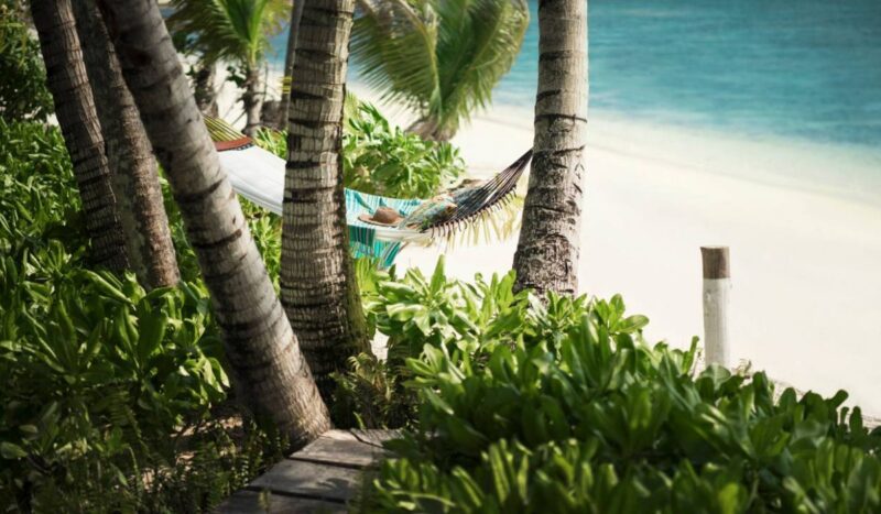 A hammock strung between palm trees on a private beach at Four Seasons Resort Seychelles at Desroches Island.