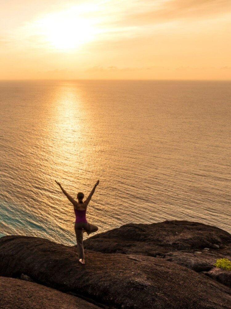 A person practising sunset yoga on a granite outcrop overlooking Petite Anse at Four Seasons Resort Seychelles.