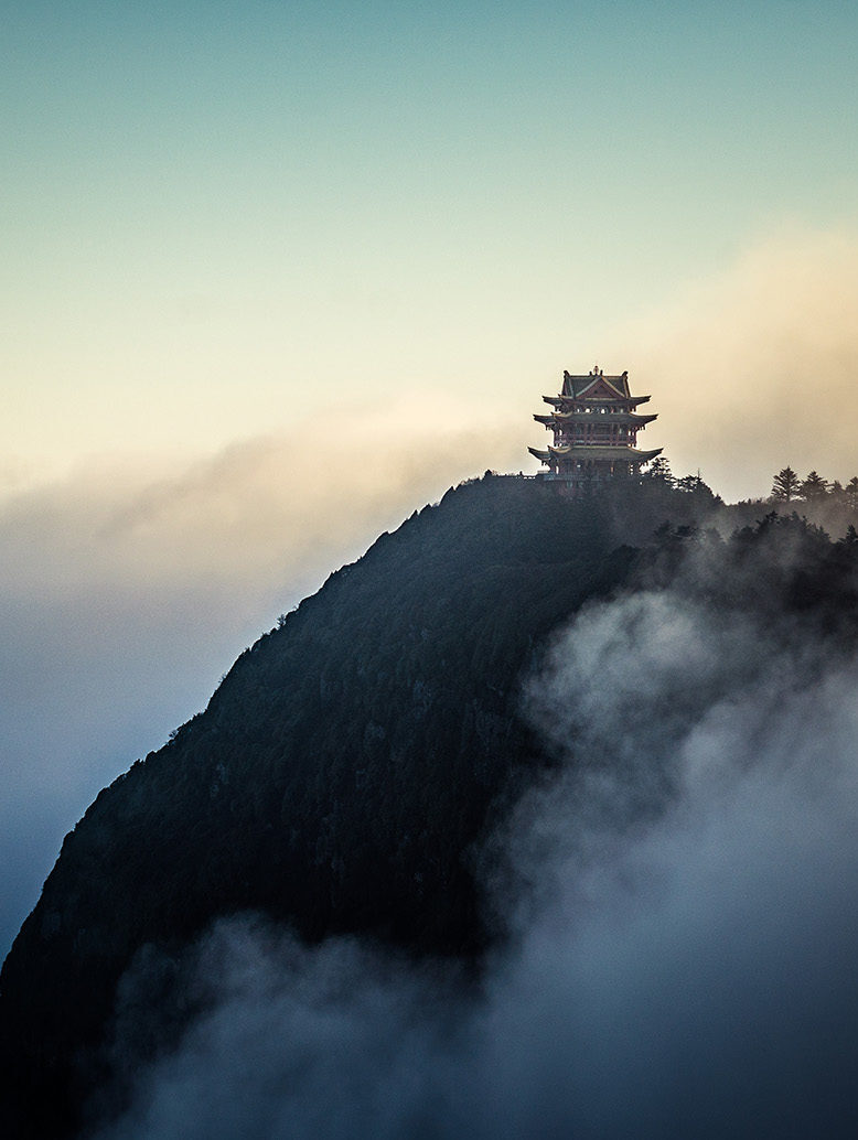 A gold-topped temple on a dark mountain peak above thick white clouds for luxury culture tours.