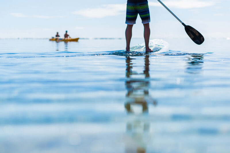 Person standing on a paddleboard in clear blue water during luxury adventure tours.