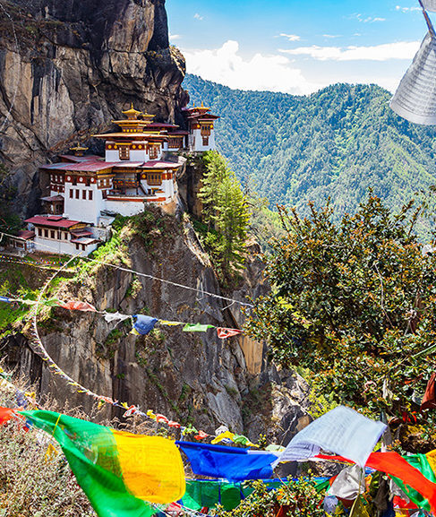 Tiger's Nest Monastery perched on a cliffside with prayer flags in the foreground for luxury asian family tours.