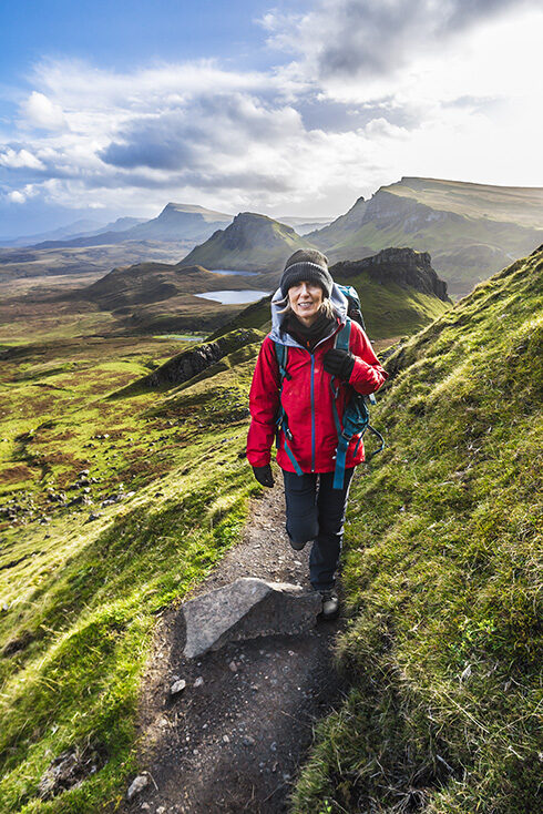 Hiker in a red jacket walking on a green mountain trail during luxury adventure tours.