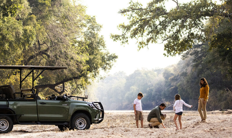A family of four standing near a green off-road vehicle in a dry riverbed on luxury African family safari trips.